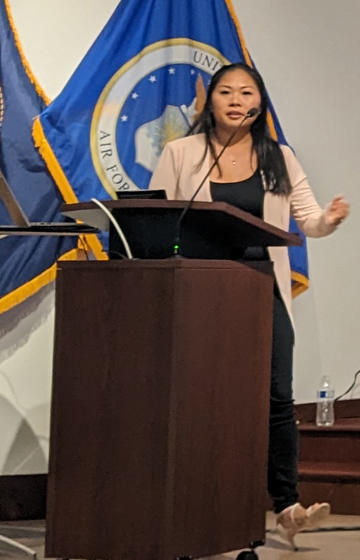 Alice Beatty stands at a podium in front of flags
