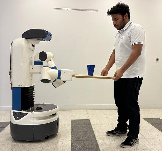 A robot and a student collaboratively carry a glass of water on a board. Photo provided.
