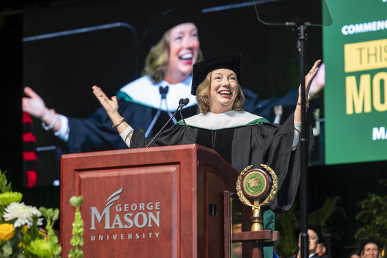 Barbara Humpton is wearing regalia and standing behind the podium on the stage in EagleBank Arena.
