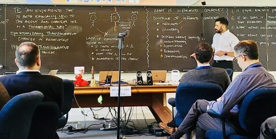 Andrew Peterson stands at the front of a classroom reviewing ethical and policy issues that are written on the chalkboard