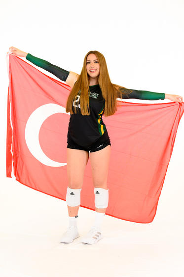Tuana Ozarpaci wears her green Mason Volleyball uniform and holds the red flag with white star and crescent of the Republic of Türkiye