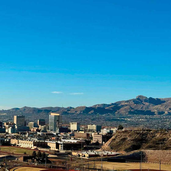 A city on the border between the US and Mexico, with another city somewhat visible across the border. Mountains dot the landscape beneath a blue sky.