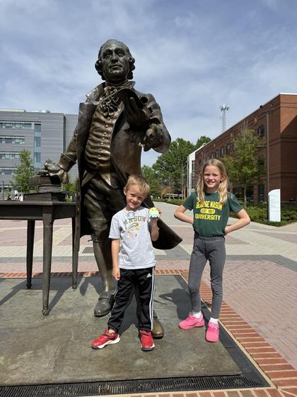 Two children stand on the pedestal at the George Mason statue on Wilkins Plaza