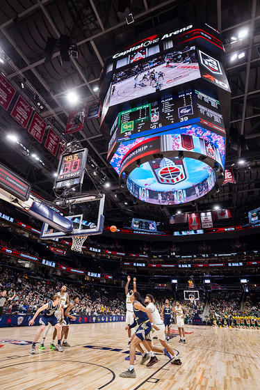 A basketball player shoots the ball towards the hoop as others rush to defend.