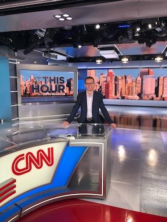 Nathan Crawford stands behind CNN's Washington DC bureau television studio desk. He smiles, wearing a sport coat and oxford shirt.