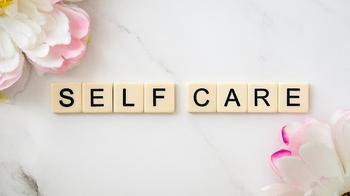 Pink and white flowers in top left and bottom right corner. In the center of the image are Scrabble letters that spell out "Self Care"