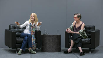 At left, composer Maria Schneider in white shirt, colorful silk scarf, and jeans, speaks to the audience, sitting next to moderator Sandra Aistars, George Mason University Antonin Scalia Law School Professor and Arts & Entertainment Advocacy Clinic Director.