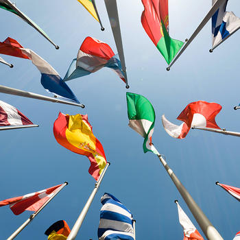 Flags from multiple countries on poles, photographed from the ground and looking up.