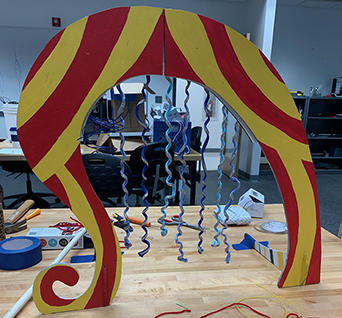 A musical rag harp sculpture. Under a large arch are dangling pieces of yarn that are made from upcycled T-shirts.
