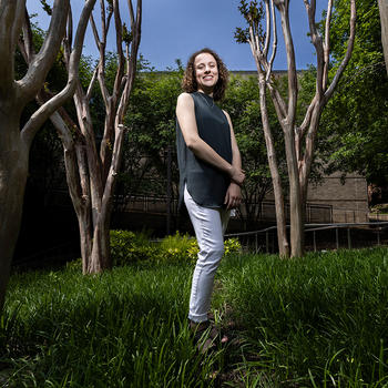 Hannah Adamson stands in the middle of a spaced group of trees outside on the Fairfax Campus of George Mason University.