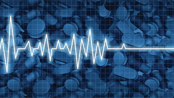 Stock image of a flatlining heart beat over a semi-visible pile of pills.