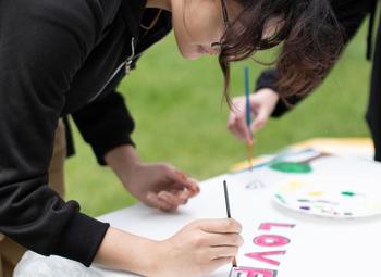 Someone paints the word "love" on a large paper at Spring into Well-Being