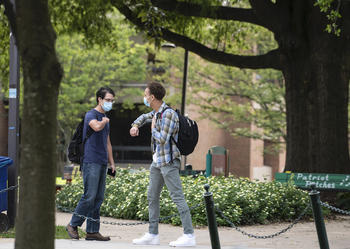 Students wearing face masks greet eachother by bumping elbows to maintain social distance during COVID19. 