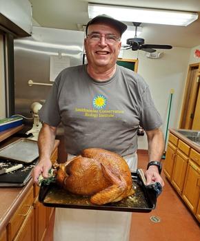 Buz Grover holds a smoked turkey in a pan in a commercial kitchen