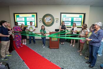 Students and faculty hold ends of a green ribbon as a student cuts the ribbon