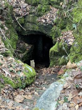 Entrance to Crystal Cave is a dark opening in a mossy cliff, with a stone staircase leading to the entrance