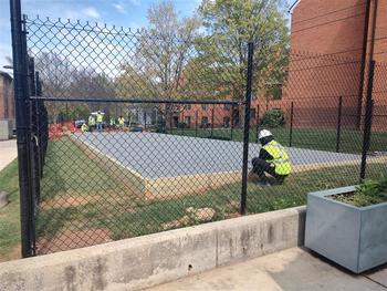 Contractors work to complete a concrete pad behind a chain link fence in Presidents Park to accommodate the solar array