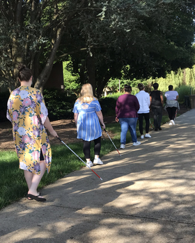 Students practice walking with sight canes on a sidewalk.