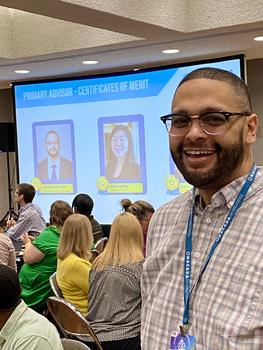 Joshua Fletcher stands in front of the presentation screen that shows a slide recognizing him for his award