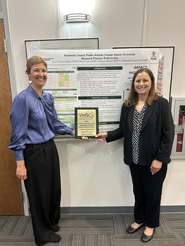 Baker (left) and Crawford pose in front of a research poster with their Program That Works plaque.